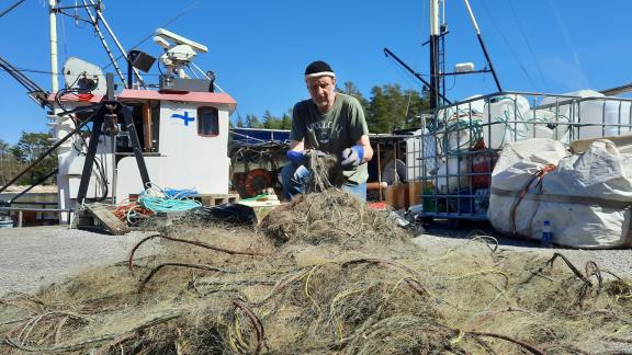 Tutkija Pekka Kotilainen puhdistaa merestä poistettuja vanhoja verkkoja kalasataman laiturilla toukokuussa 2024.