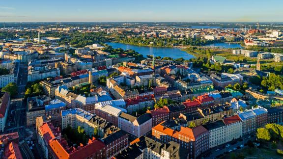 Ilmakuva tiiveistä kaupunkikortteleista, punakattoisista ja vaaleista kerrostaloista. Taustalla näkyy vesialuetta ja puistoja.