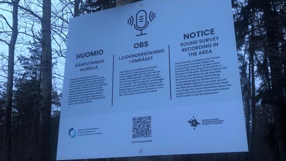 Tiedotuskyltti paikan päällä tapahtuvasta äänimaisematutkimuksesta metsässä.