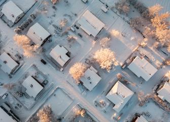 Ilmakuva talvisesta omakotialueesta suoraan ylhäältäpäin. Kuvassa näkyy ruutukaavaan sijoitettujen rakennusten lumisia kattoja.