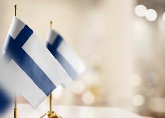 Kuvassa vasemmalla näkyy pieniä Suomen lippuja rivissä asetettuna pöydälle. Tausta on sumennetty.