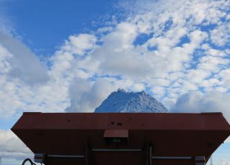 Kipsiä kuormurin kauhassa levitystä varten. Taustalla sininen taivas ja pilviä. Gypsum in a loader bucket ready for field application. Blue sky and clouds in the background.
