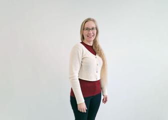Kaisa Raatikainen smiles at the camera. She is wearing a white sweater and black trousers.