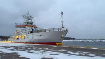 Lights from the deck of the research vessel Aranda shine into the grey winter morning dockscape in January 2026.