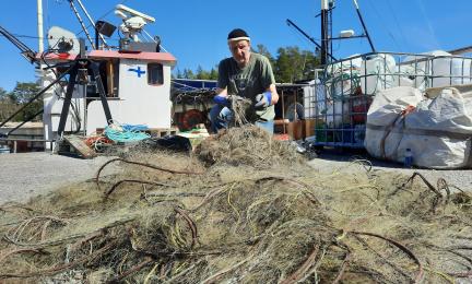 Vanhempi tutkija Pekka Kotilainen istuu kalasatamassa laiturialueella siivoamassa merestä nostettuja haamuverkkoja aurinkoisena kevätpäivänä. 