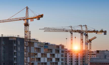 Useita nostureita työskentelee kerrostalojen rakennustyömaalla auringonlaskun aikaan.