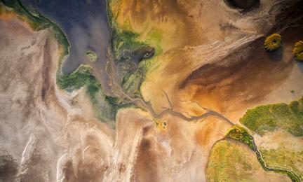 Picture of a river basin taken from above, the surrounding environment is arid with sand.