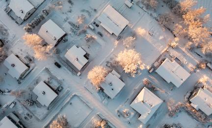 Ilmakuva talvisesta omakotialueesta suoraan ylhäältäpäin. Kuvassa näkyy ruutukaavaan sijoitettujen rakennusten lumisia kattoja.