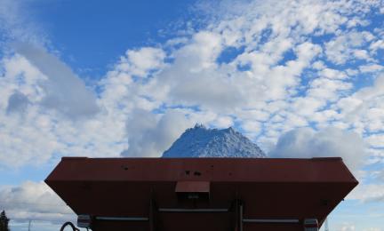 Kipsiä kuormurin kauhassa levitystä varten. Taustalla sininen taivas ja pilviä. Gypsum in a loader bucket ready for field application. Blue sky and clouds in the background.