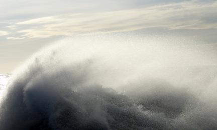 Itämeren aalto hajoaa miljooniksi pisaroiksi, taustalla näkyy ohut pilvistä vaaleansinistä taivasta.
