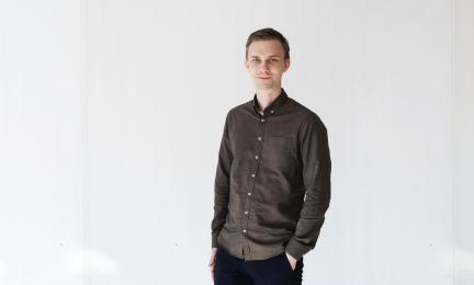 Mikko Impiö seisoo kameraa kohti, kädet taskuissa, päällään ruskea kauluspaita ja mustat housut.